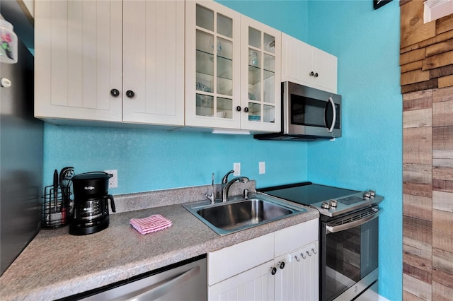 kitchen featuring white cabinets, glass insert cabinets, appliances with stainless steel finishes, and a sink