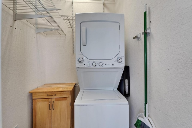 laundry area featuring cabinet space, a textured wall, and stacked washer / dryer