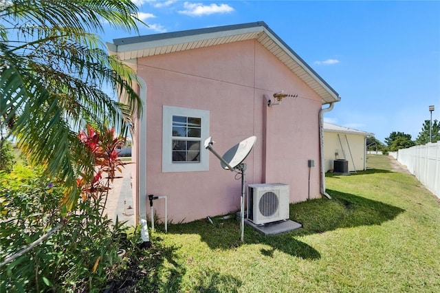 view of side of home with central air condition unit, fence, ac unit, a yard, and stucco siding