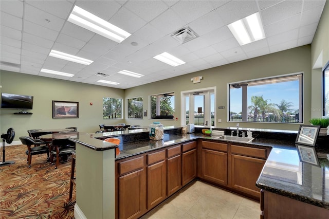 kitchen featuring a peninsula, a sink, dark stone countertops, visible vents, and brown cabinets