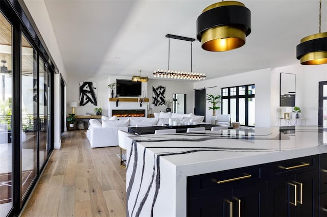 kitchen with light wood-type flooring, hanging light fixtures, open floor plan, and dark cabinetry