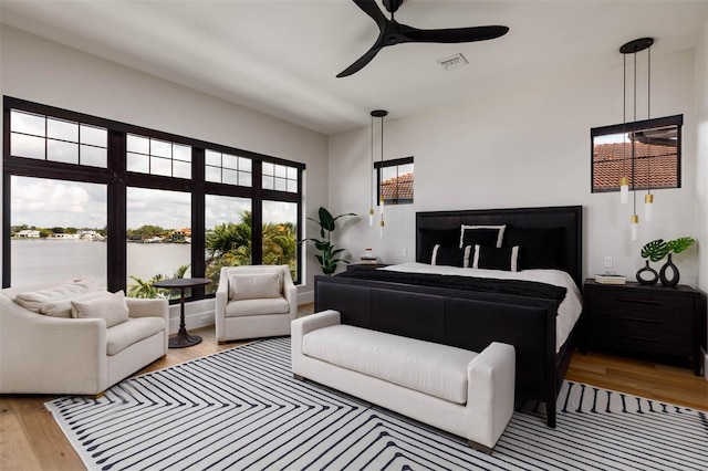 bedroom featuring wood finished floors, a ceiling fan, visible vents, and a water view