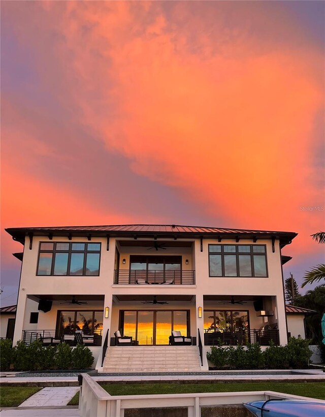 back of property at dusk with a standing seam roof, a ceiling fan, a balcony, and stucco siding