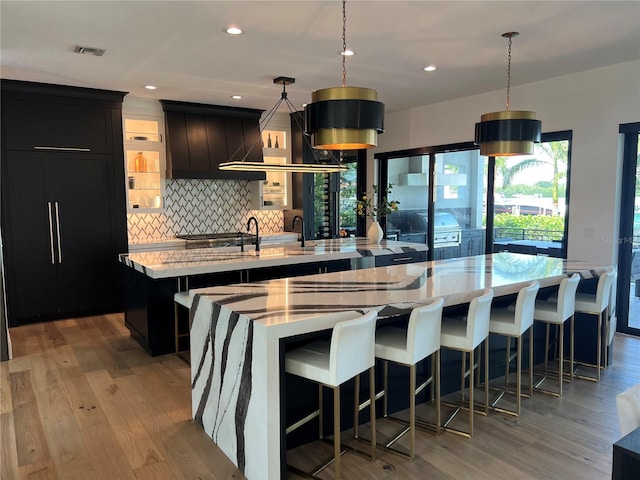 kitchen featuring light wood-style flooring, a spacious island, backsplash, and dark cabinetry