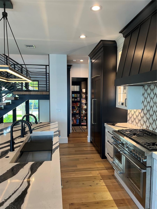 kitchen with tasteful backsplash, custom exhaust hood, a sink, range with two ovens, and visible vents