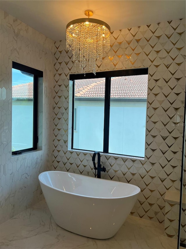 bathroom featuring a soaking tub, a notable chandelier, marble finish floor, and tile walls