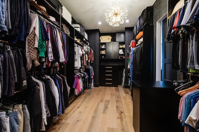 walk in closet with light wood finished floors and a notable chandelier