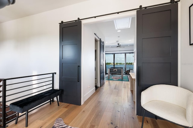 hall featuring a barn door, recessed lighting, light wood finished floors, and baseboards
