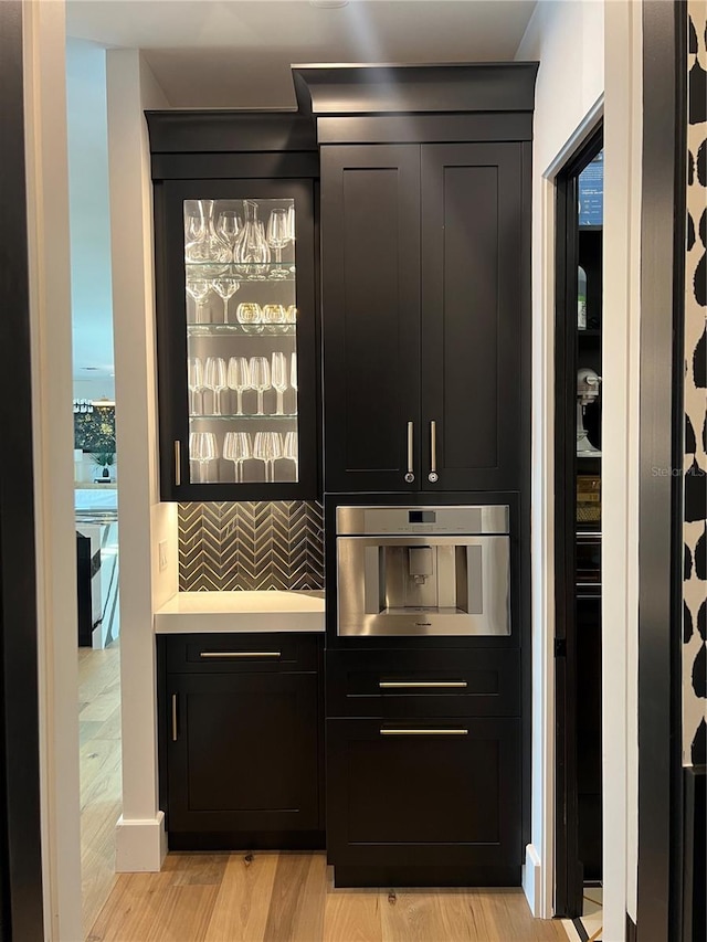 bar featuring backsplash, stainless steel oven, and light wood-style flooring