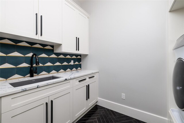kitchen with light stone counters, white cabinets, backsplash, a sink, and baseboards