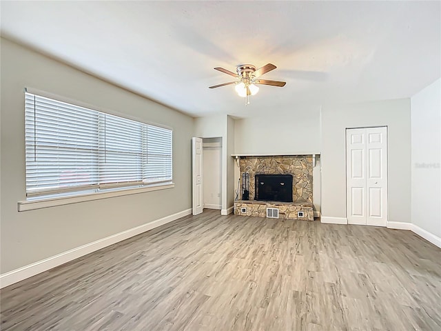unfurnished living room featuring baseboards, visible vents, a stone fireplace, ceiling fan, and wood finished floors