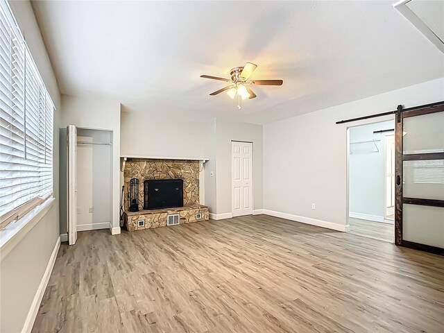 unfurnished living room with light wood-type flooring, a stone fireplace, a barn door, and ceiling fan