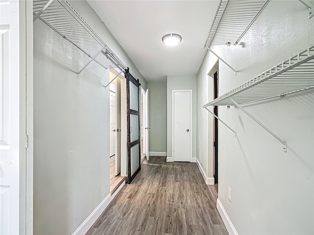 hallway featuring baseboards, a barn door, and wood finished floors