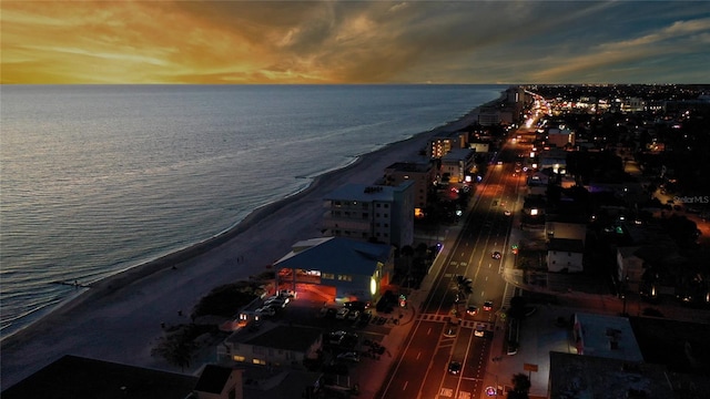 aerial view at dusk featuring a water view and a view of the beach
