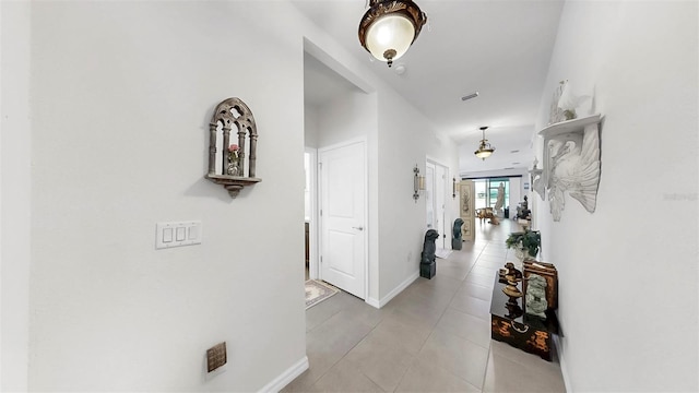 hall with baseboards, visible vents, and light tile patterned floors
