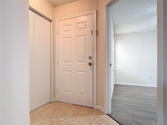 entryway with light tile patterned floors, baseboards, and a textured ceiling