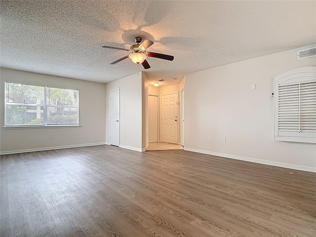 empty room with dark wood-style flooring, baseboards, a textured ceiling, visible vents, and a ceiling fan