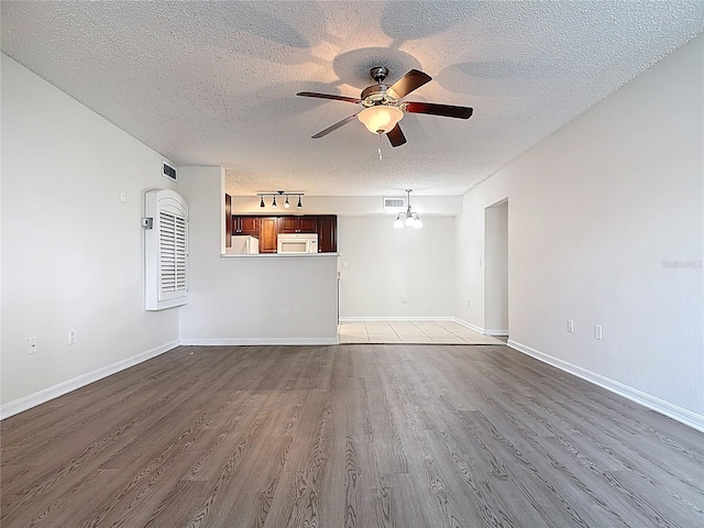 unfurnished living room with a textured ceiling, visible vents, baseboards, ceiling fan, and wood finished floors