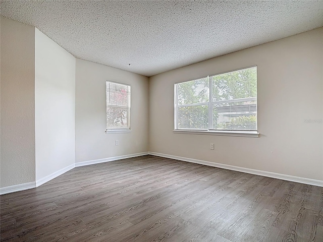 unfurnished room with dark wood-type flooring, a textured ceiling, and baseboards
