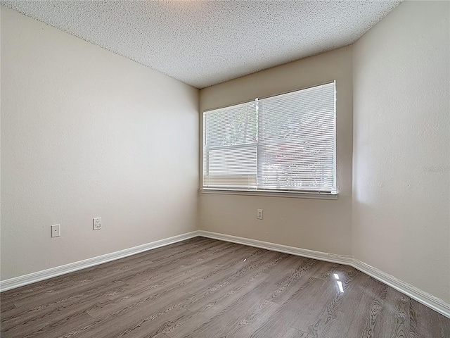 unfurnished room featuring baseboards, wood finished floors, and a textured ceiling