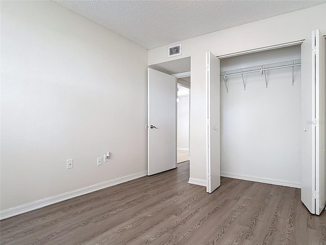 unfurnished bedroom featuring a closet, a textured ceiling, visible vents, and wood finished floors