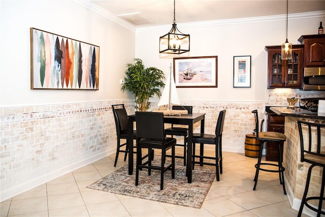 dining area with crown molding, light tile patterned floors, a chandelier, wainscoting, and tile walls