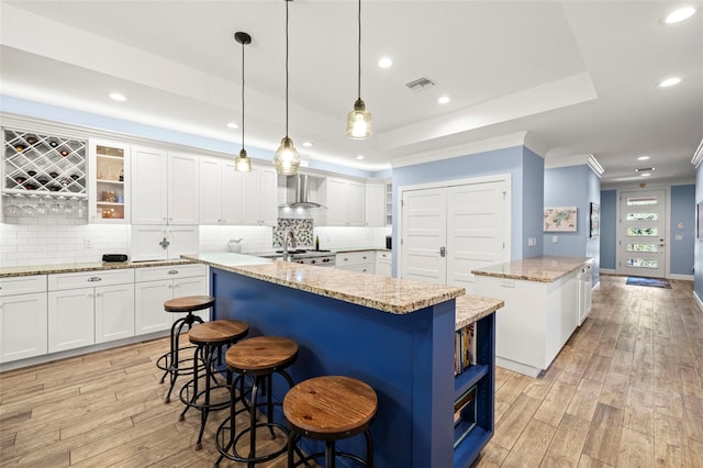 2623 57th St S, Gulfport, FL 33707 - kitchen featuring a kitchen island, light wood-style floors, wall chimney exhaust hood, a tray ceiling, and visible vents