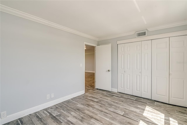 unfurnished bedroom featuring visible vents, baseboards, a closet, ornamental molding, and wood finished floors