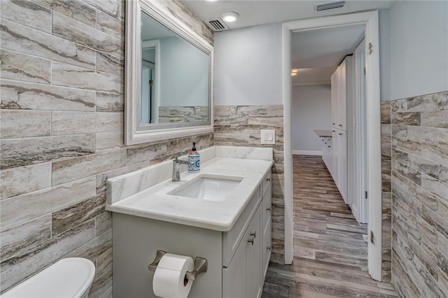 half bath with vanity, visible vents, toilet, wood finished floors, and tile walls