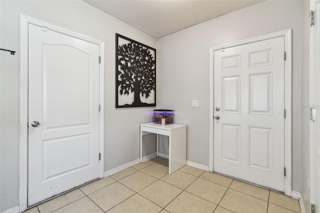 entrance foyer with light tile patterned floors, a textured ceiling, and baseboards