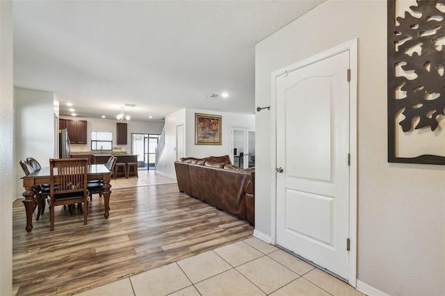 interior space featuring freestanding refrigerator, light tile patterned floors, dark brown cabinets, open floor plan, and baseboards