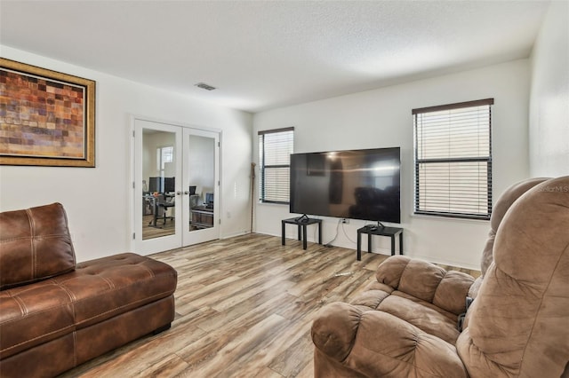 living area with french doors, a textured ceiling, visible vents, and wood finished floors