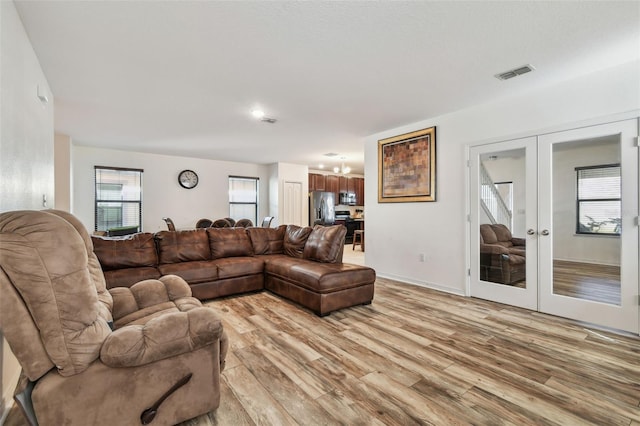 living area featuring french doors, visible vents, light wood finished floors, and a notable chandelier