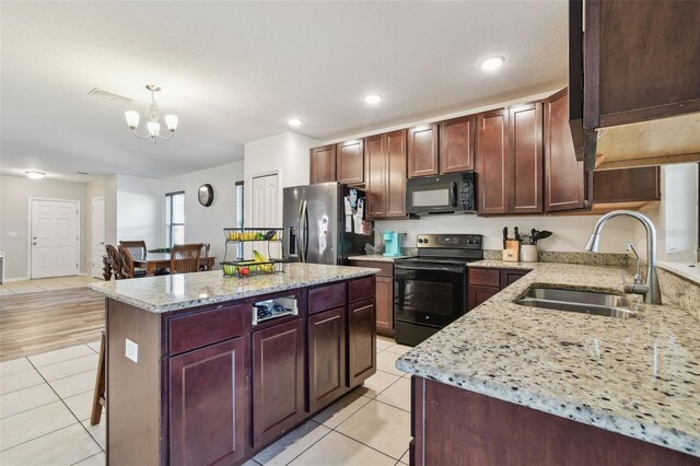 kitchen featuring light tile patterned floors, a notable chandelier, a sink, black appliances, and light stone counters