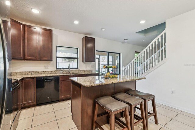 kitchen with dishwasher, a sink, a breakfast bar, light stone countertops, and light tile patterned flooring