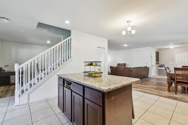 kitchen featuring an inviting chandelier, light stone countertops, a kitchen island, light tile patterned flooring, and open floor plan