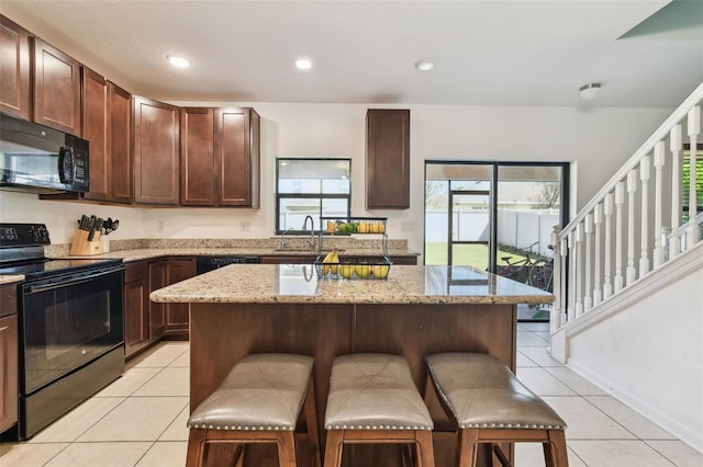 kitchen with a kitchen bar, black appliances, a center island, light tile patterned flooring, and a sink