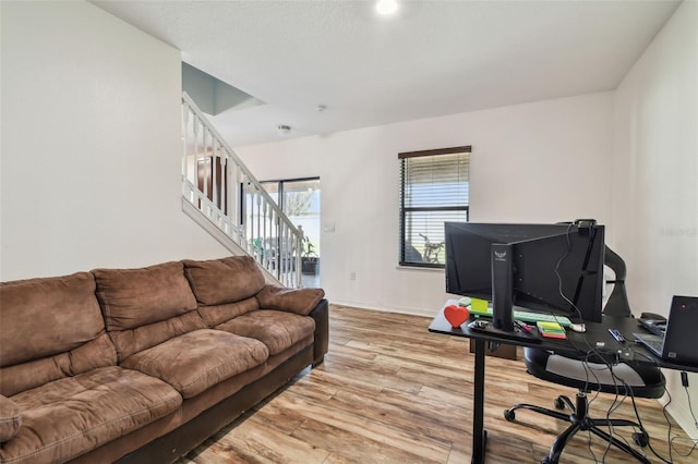 living area with baseboards, stairway, and light wood-style floors