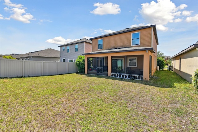rear view of house with fence, a sunroom, a lawn, and stucco siding