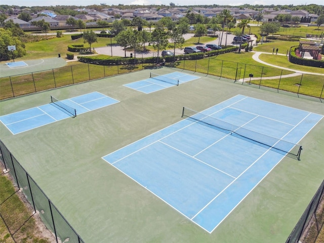 view of tennis court with a residential view, fence, and a yard