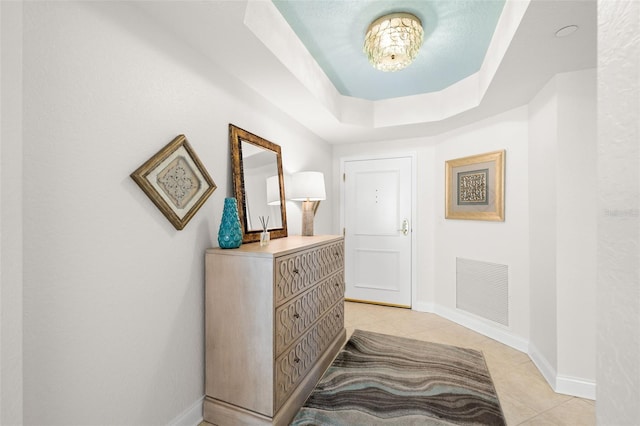 hallway featuring light tile patterned floors, a tray ceiling, and baseboards