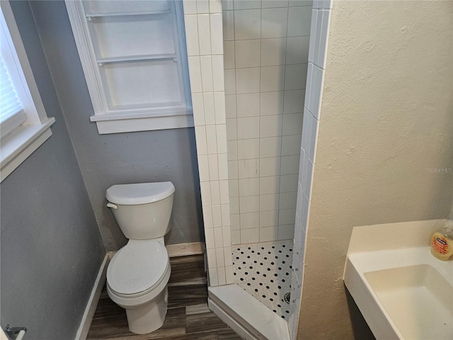 bathroom with baseboards, a textured wall, toilet, a tile shower, and wood finished floors