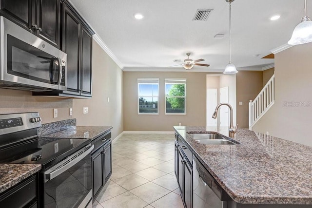 kitchen with a sink, a center island with sink, stainless steel appliances, visible vents, and ornamental molding