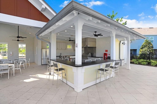 view of patio with an outdoor bar, area for grilling, fence, and a ceiling fan