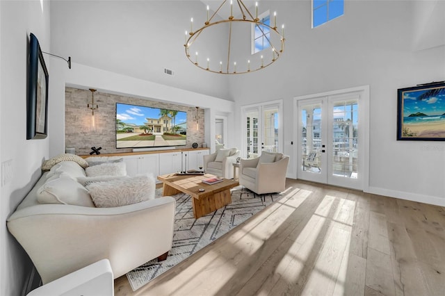 living area featuring visible vents, an inviting chandelier, a towering ceiling, wood finished floors, and french doors