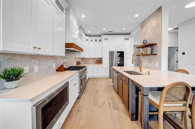 kitchen with light stone countertops, open shelves, custom exhaust hood, appliances with stainless steel finishes, and a sink