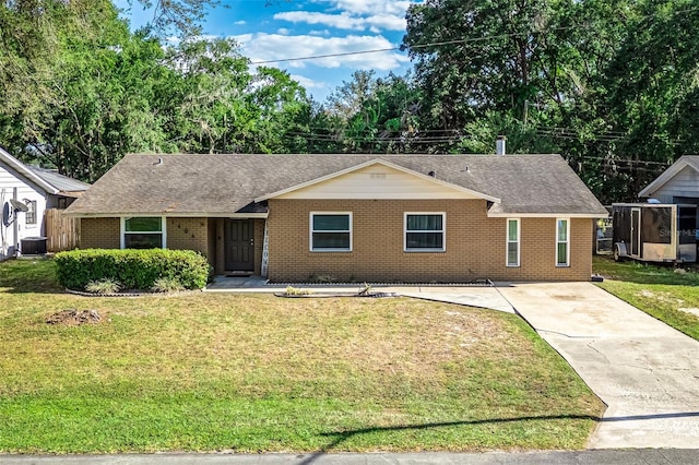 single story home with driveway, a front yard, roof with shingles, brick siding, and central AC