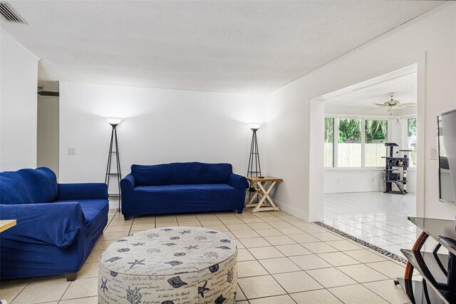 living area featuring light tile patterned flooring, a textured ceiling, visible vents, baseboards, and a ceiling fan