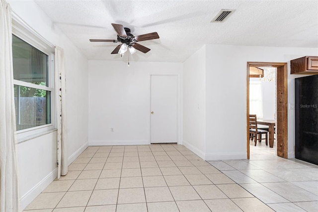 empty room with light tile patterned flooring, a textured ceiling, visible vents, baseboards, and a ceiling fan