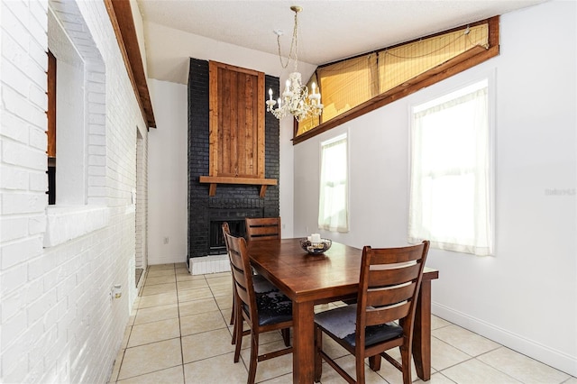 dining room with a brick fireplace, light tile patterned floors, brick wall, and a notable chandelier